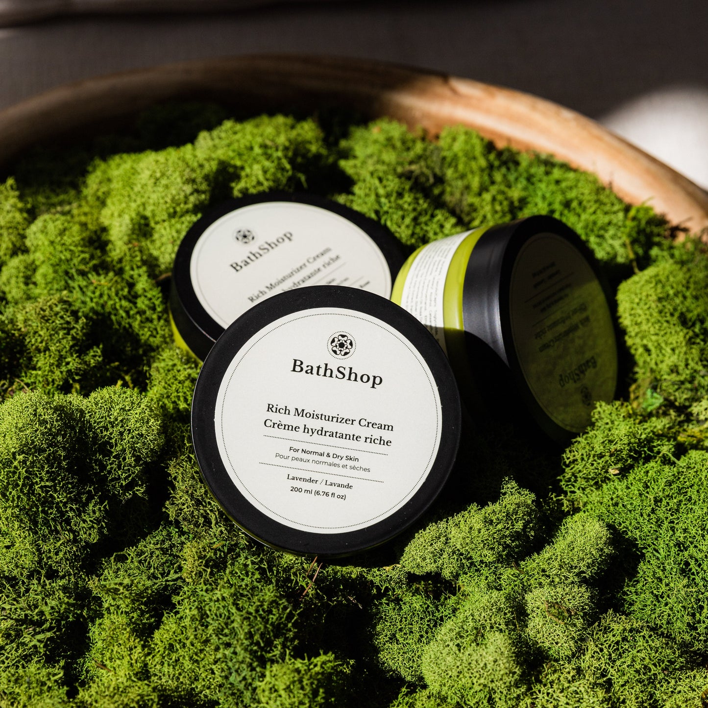 Plant-based moisturizer cream from The Bath Shop on a bed of green moss in a wooden bowl.