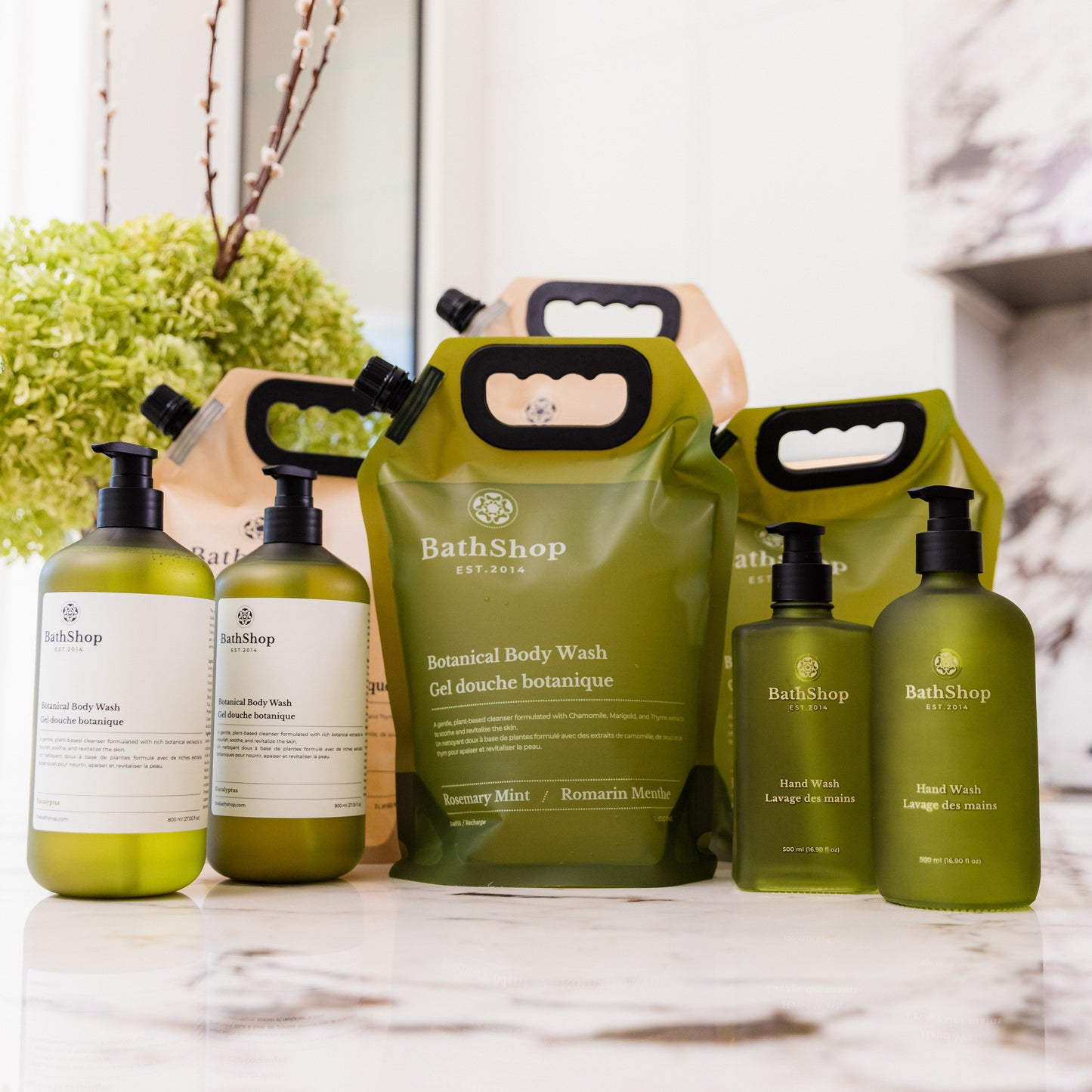 Plant-based collection of The Bath Shop products including bottles and eco-friendly refill bags on a marble surface.
