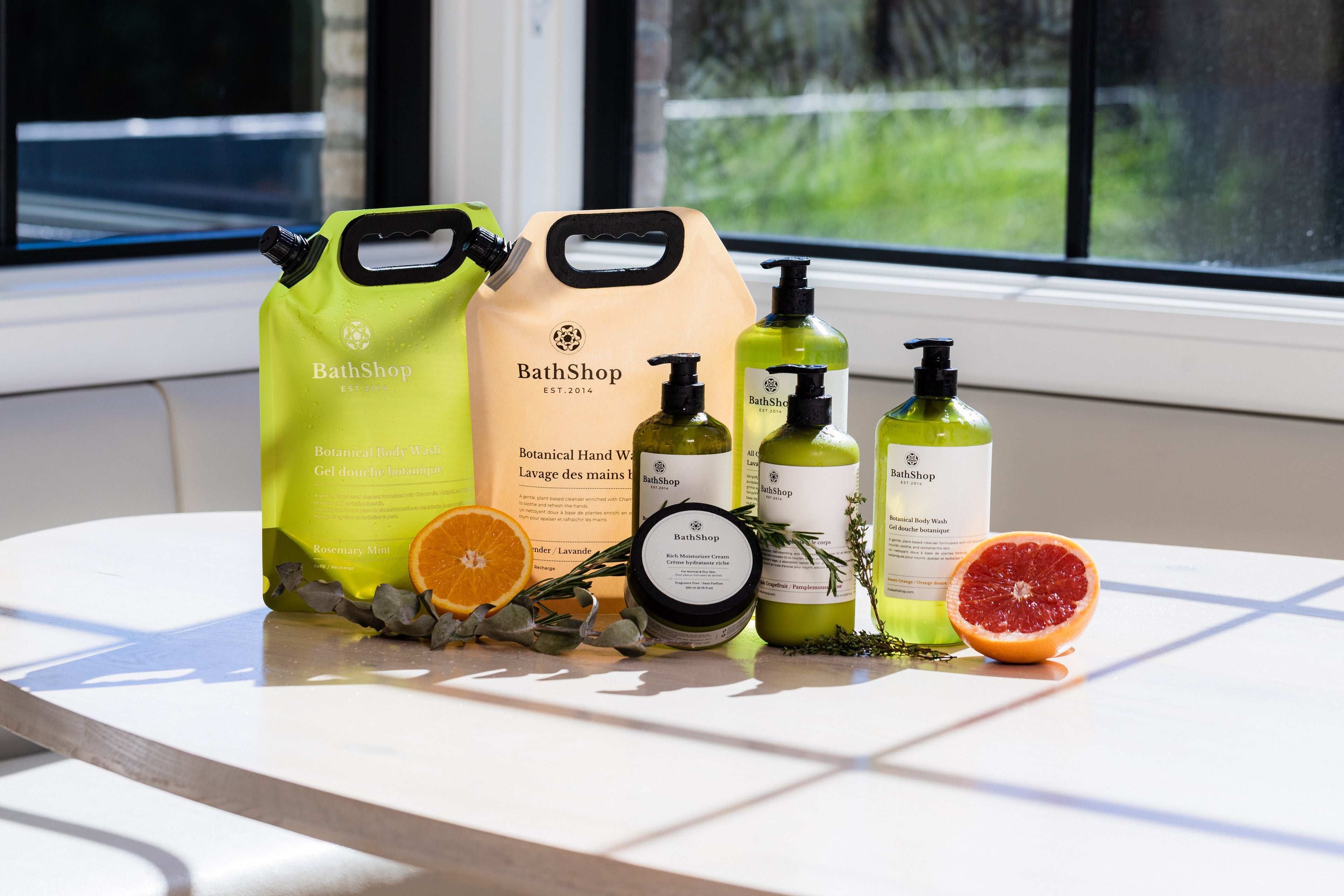 The Bath Shop products including bags, bottles, and a bar of soap on a table with fruits.