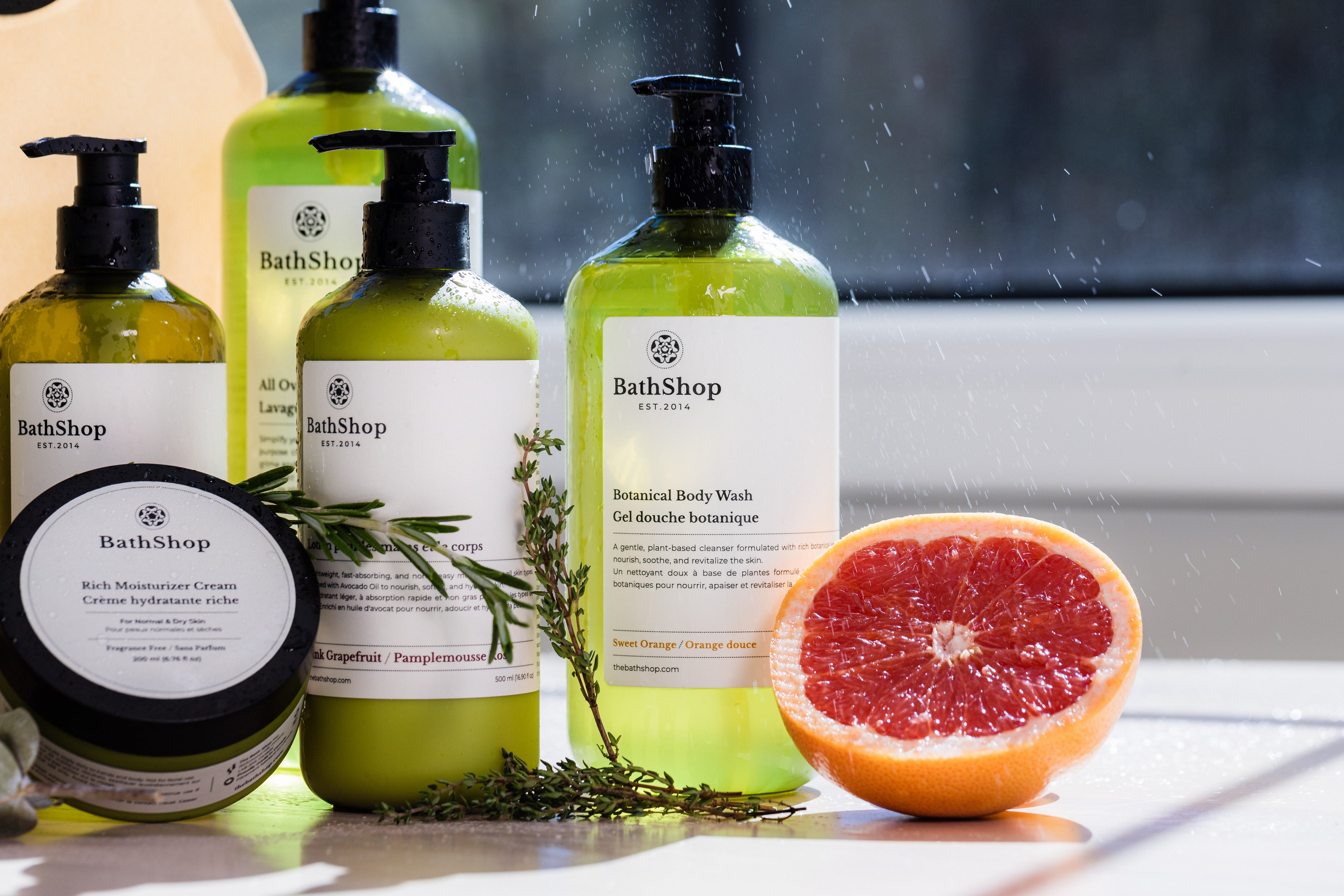 The Bath Shop products including bottles and a grapefruit on a reflective surface.