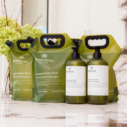 Plant-based and eco-friendly  products by The Bath Shop including bottles and pouches on a marble surface with a blurred background.