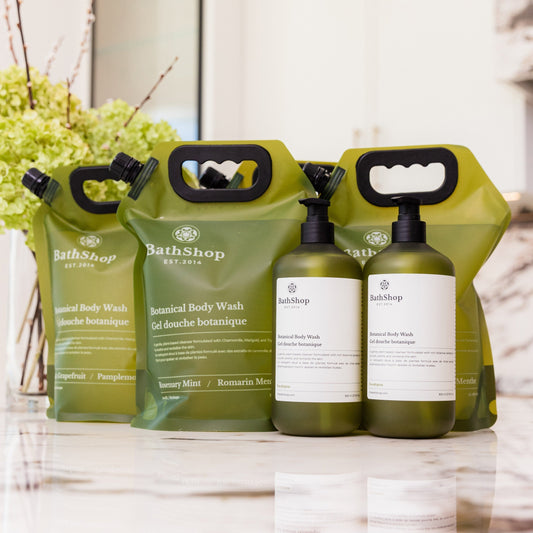 Plant-based and eco-friendly  products by The Bath Shop including bottles and pouches on a marble surface with a blurred background.